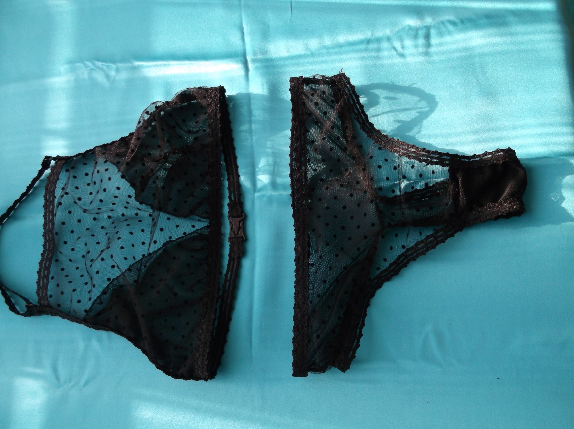 Damska bielizna: czarne, koronkowe majtki z tiulu w kropki, rozłożone na turkusowym, satynowym tle.