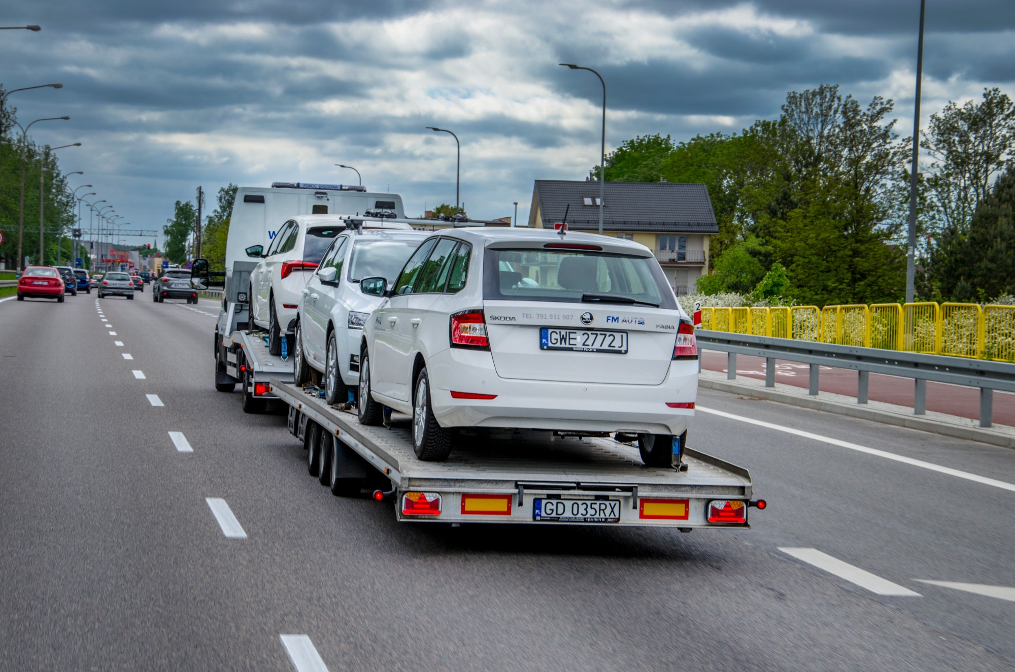 Laweta transportuje trzy białe samochody osobowe Skoda na autostradzie, widok z tyłu, tablice rejestracyjne widoczne.