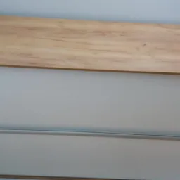 Fragment szafy przesuwnej z białymi frontami i drewnianym blatem w ciepłym odcieniu, widoczne detale metalowych prowadnic.