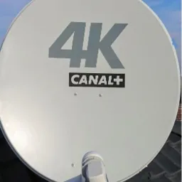 Biała antena satelitarna 4K Canal+ zamontowana na dachu z ciemnej dach&oacute;wki, widoczna z bliska.
