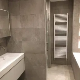 Nowoczesna łazienka w odcieniach szarości z białymi elementami armatury, w tym grzejnikiem drabinkowym i umywalką nablatową.