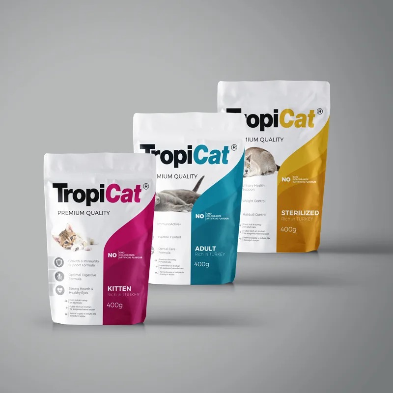 Trzy opakowania karmy dla kotów TropiCat: Kitten, Adult i Sterilized, ustawione w rzędzie na szarym tle, z różnymi kolorami i grafikami dla każdej kategorii wiekowej.