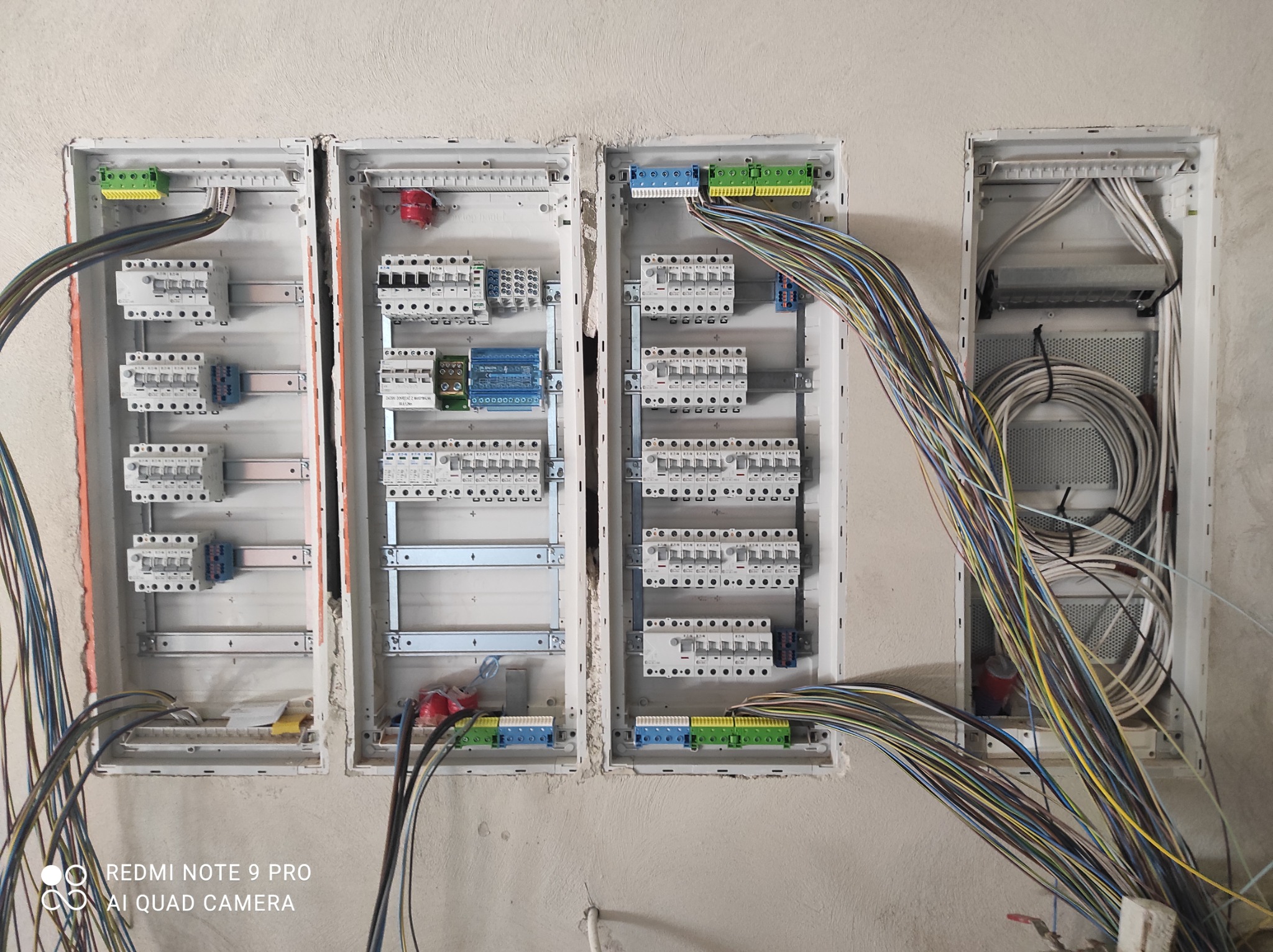Rozdzielnice elektryczne w trakcie montażu, widoczne liczne przewody, zabezpieczenia i listwy zaciskowe, ściana w stanie surowym.