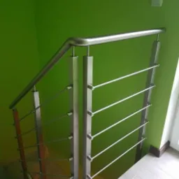 Nowoczesna balustrada ze stali nierdzewnej z poziomymi prętami, mocowana do schod&oacute;w, na tle jaskrawozielonej ściany z białym włącznikiem światła.