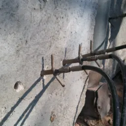 Betonowa ściana z nawierconymi otworami i zainstalowanymi iniektorami podłączonymi do przewodów iniekcyjnych, prawdopodobnie w trakcie osuszania lub wzmacniania konstrukcji.