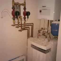 Nowa instalacja kotła gazowego Vaillant z widocznymi pompami obiegowymi i rozdzielaczem podłogówki w trakcie montażu, zabezpieczona folią ochronną.