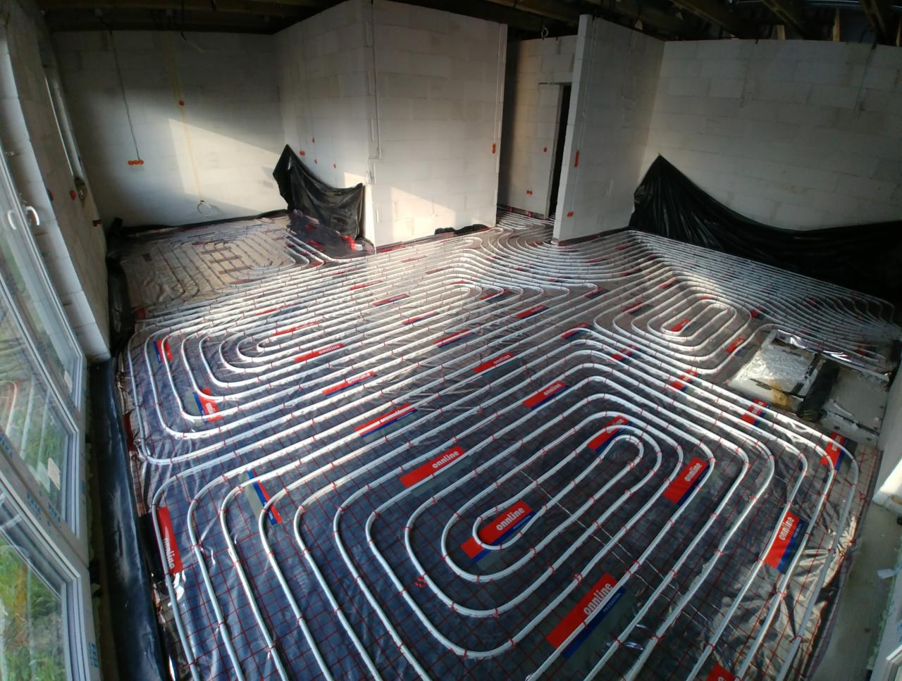 Białe rurki ogrzewania podłogowego ułożone w pętle na izolacji, widok z góry na surowy stan wykończenia wnętrza.