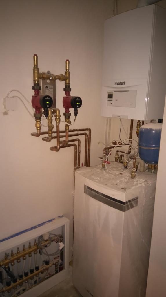 Nowa instalacja kotła gazowego Vaillant z widocznymi pompami obiegowymi i rozdzielaczem podłogówki w trakcie montażu, zabezpieczona folią ochronną.