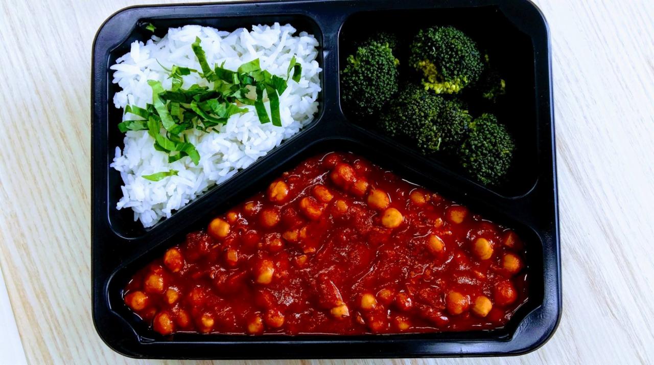 Posiłek w czarnym pojemniku: ryż z zielonymi ziołami, brokuły i ciecierzyca w sosie pomidorowym.