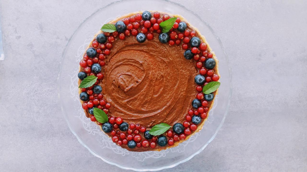 Tarta z czekoladowym kremem, borówkami, czerwoną porzeczką i listkami mięty na szklanym talerzu, widok z góry.