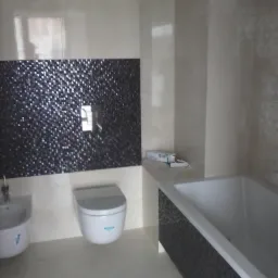 Wykończona łazienka z białą ceramiką, mozaiką w odcieniach szarości i beżowymi płytkami podłogowymi. Widoczny bidet, toaleta podwieszana i wanna obudowana mozaiką.