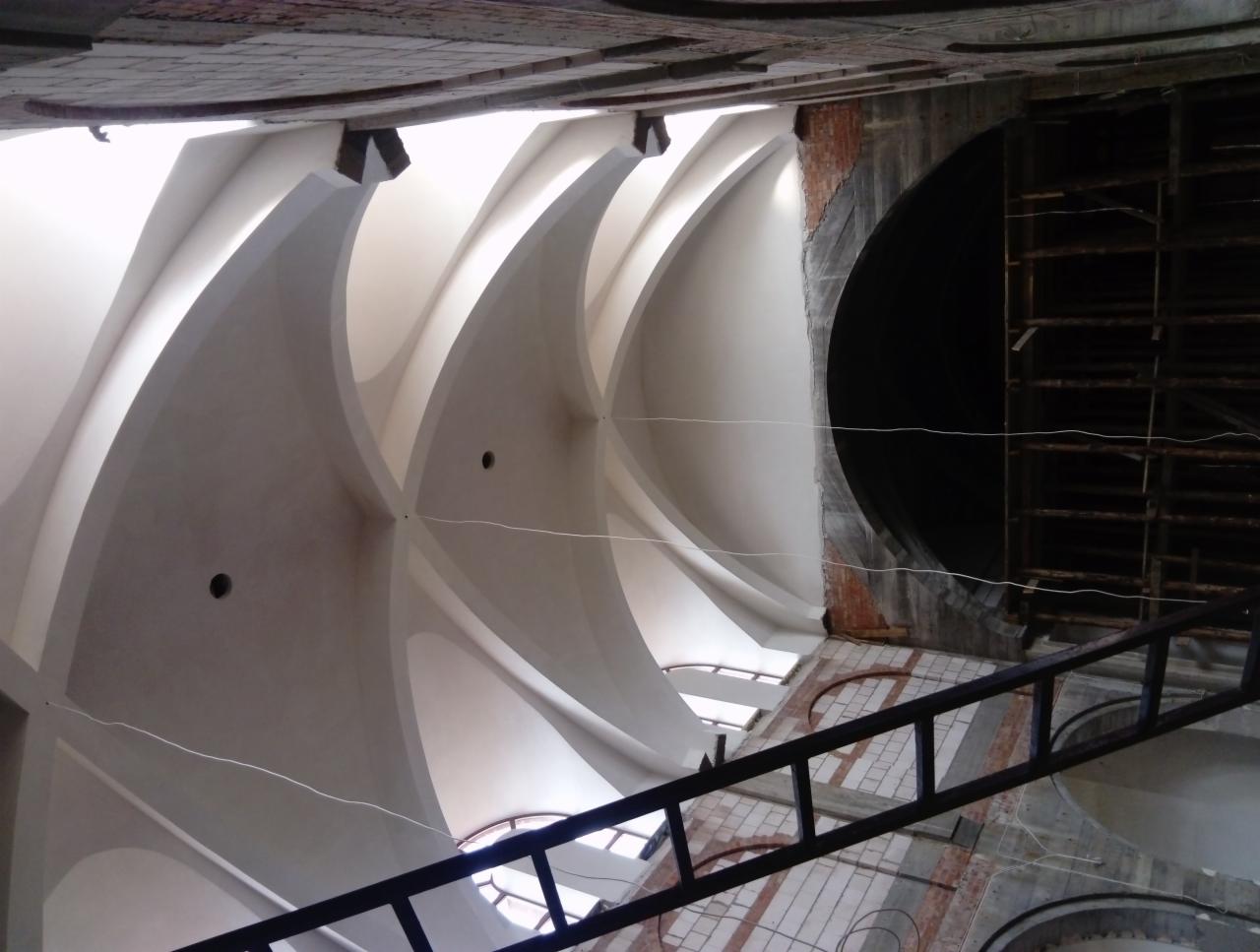 Wnętrze kościoła w trakcie renowacji, widok na sklepienie z dekoracyjnymi łukami i rusztowaniami, fragment ściany z odsłoniętą cegłą.