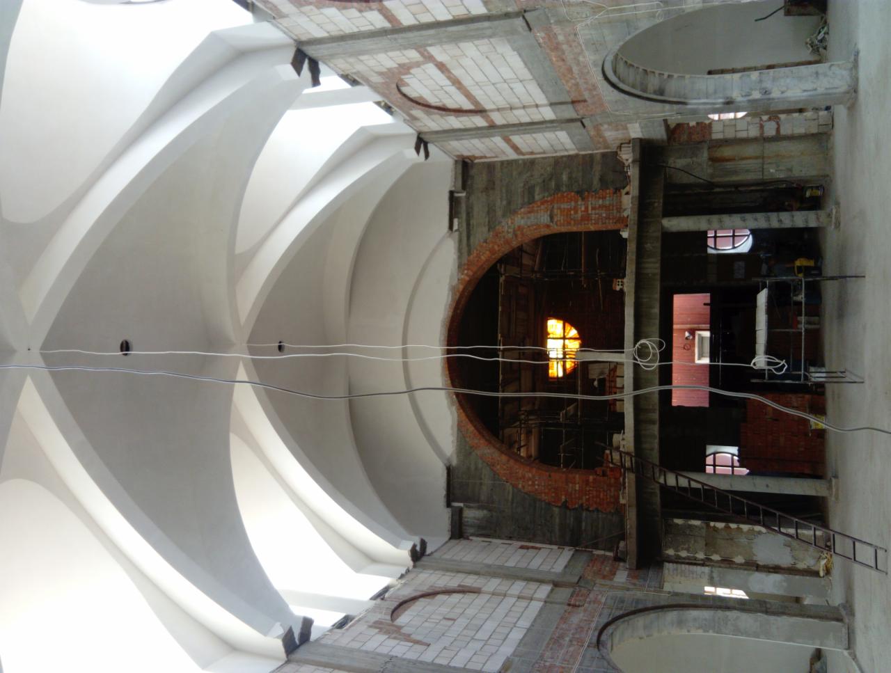 Wnętrze budynku w trakcie renowacji, widoczne sklepienie łukowe z elementami sztukaterii, ceglane łuki okienne w rusztowaniach, przewody elektryczne i drabina.