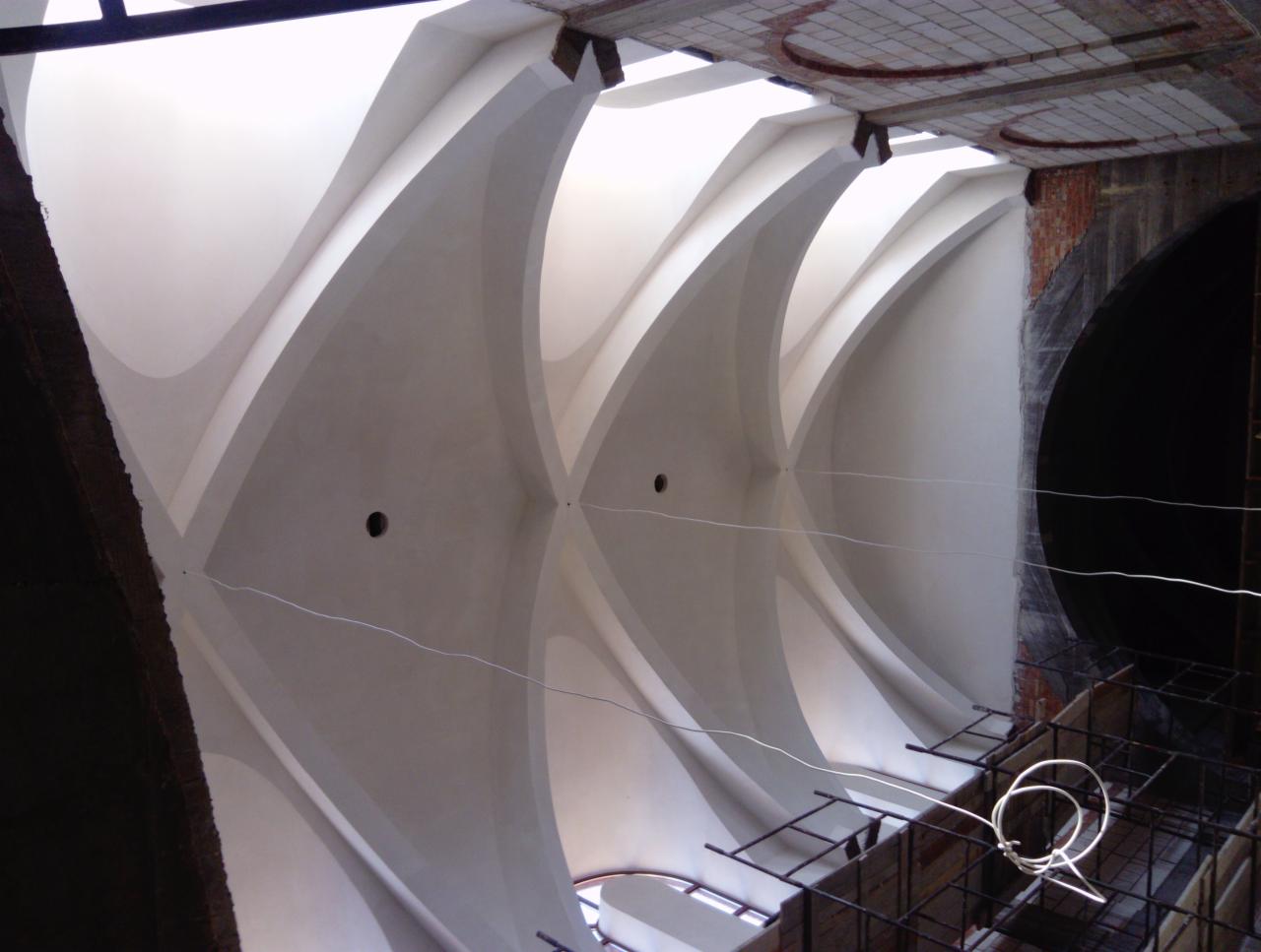 Sufit z łukami w trakcie renowacji, widoczne fragmenty starej cegły, okrągłe otwory i elementy konstrukcyjne rusztowania.