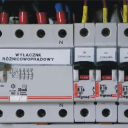Szczegółowe ujęcie tablicy rozdzielczej z wyłącznikiem różnicowoprądowym i bezpiecznikami automatycznymi marki Legrand, opisane obwody sypialni i obwód oznaczony 'Dziecinny 1'.