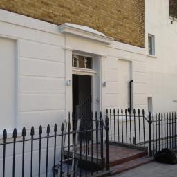 Propainting Sp z.o.o - Odnowiona fasada kamienicy z elementami dekoracyjnymi, świeżo pomalowana na biało, z czarnym kutym ogrodzeniem i widoczną drabiną przy wejściu.