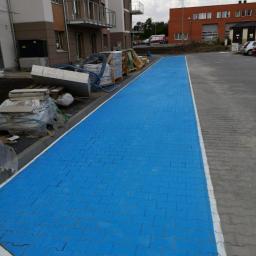 Propainting Sp z.o.o - Świeżo ułożona, jaskrawo niebieska kostka brukowa na chodniku przed nowym budynkiem mieszkalnym, z widocznymi materiałami budowlanymi w tle.