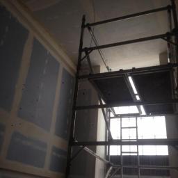 Propainting Sp z.o.o - Wnętrze w trakcie remontu: ściana z płyt gipsowo-kartonowych, widoczne łączenia szpachlowane, metalowe rusztowanie przy ścianie, okno w tle.