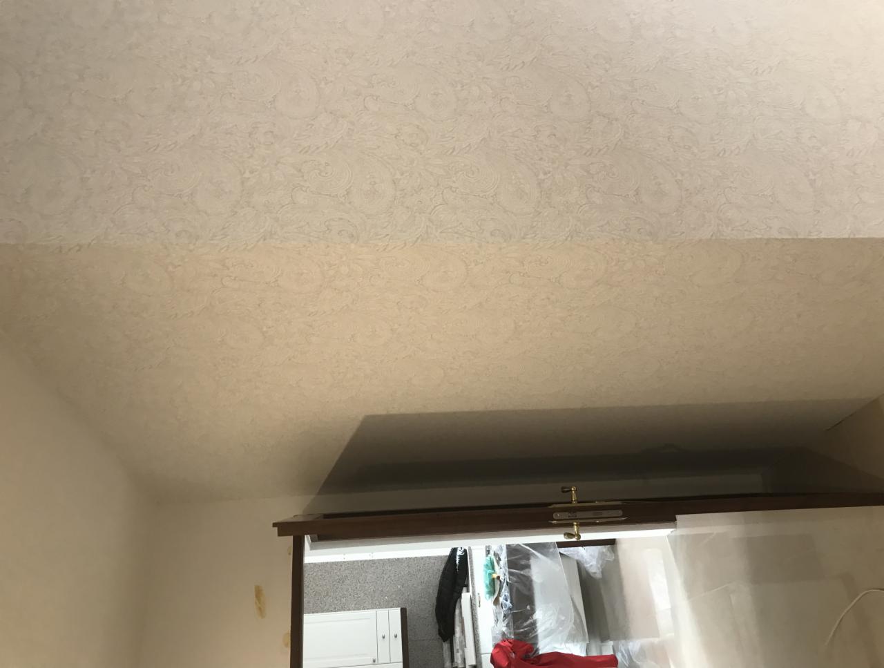 Jasny sufit z wzorzystą tapetą w odcieniach beżu, widok z dołu, fragment ściany i górna część drzwi przesuwnych z widocznym wnętrzem szafy.