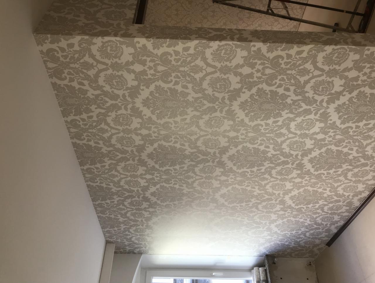 Wzorzysta tapeta w odcieniach beżu i szarości na suficie, widok z dołu, fragment okna i ściany w tle.