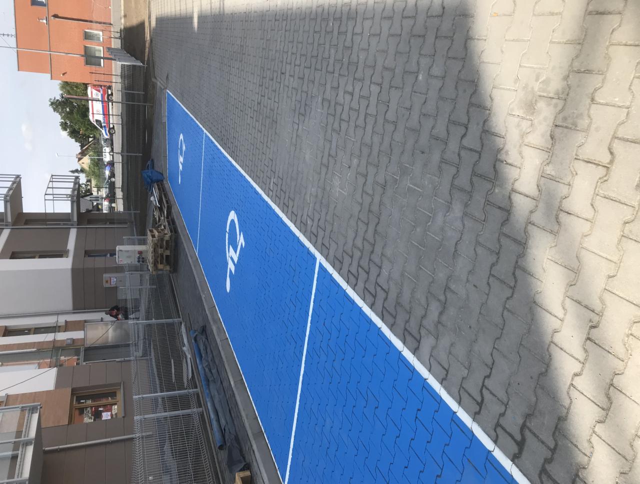 Niebieskie miejsca parkingowe dla niepełnosprawnych, świeżo pomalowane na kostce brukowej, widok z góry pod kątem.