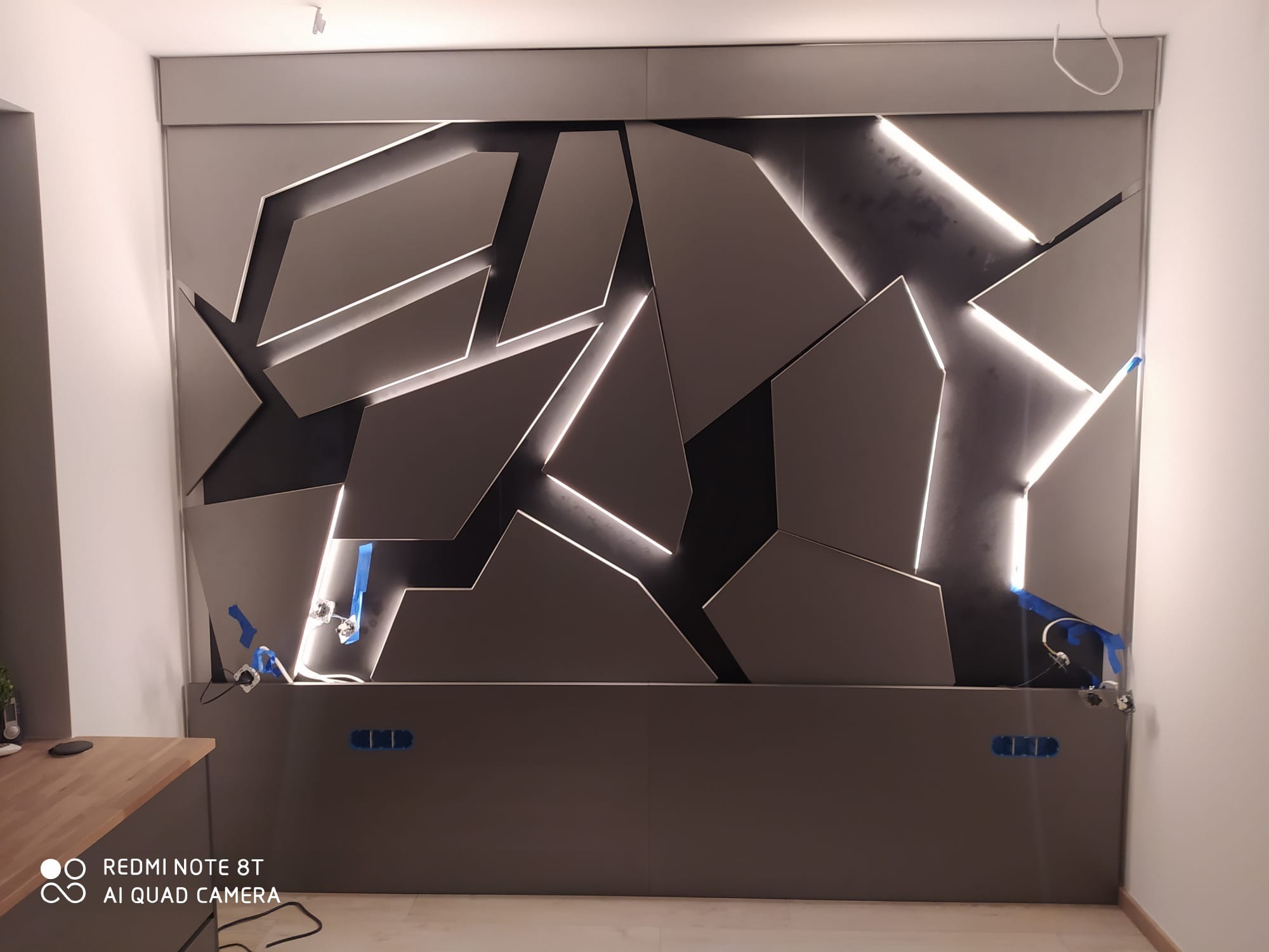 Ściana w sypialni z antracytowej płyty meblowej z geometrycznymi elementami 3D z lakierowanej płyty MDF, podświetlona LED Multi White ze sterowaniem aplikacją, widoczne niedokończone podłączenia...