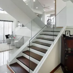 Nowoczesne schody drewniane z białymi stopnicami i szklaną balustradą, widok z dołu, jasne wnętrze z elementami dekoracyjnymi.