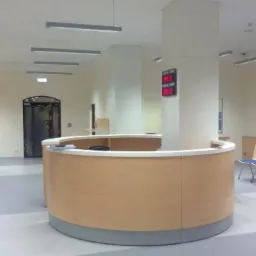 Jasne, przestronne wnętrze biura z recepcją o zaokrąglonym kształcie, rzędem krzeseł dla klientów i nowoczesnym oświetleniem sufitowym.