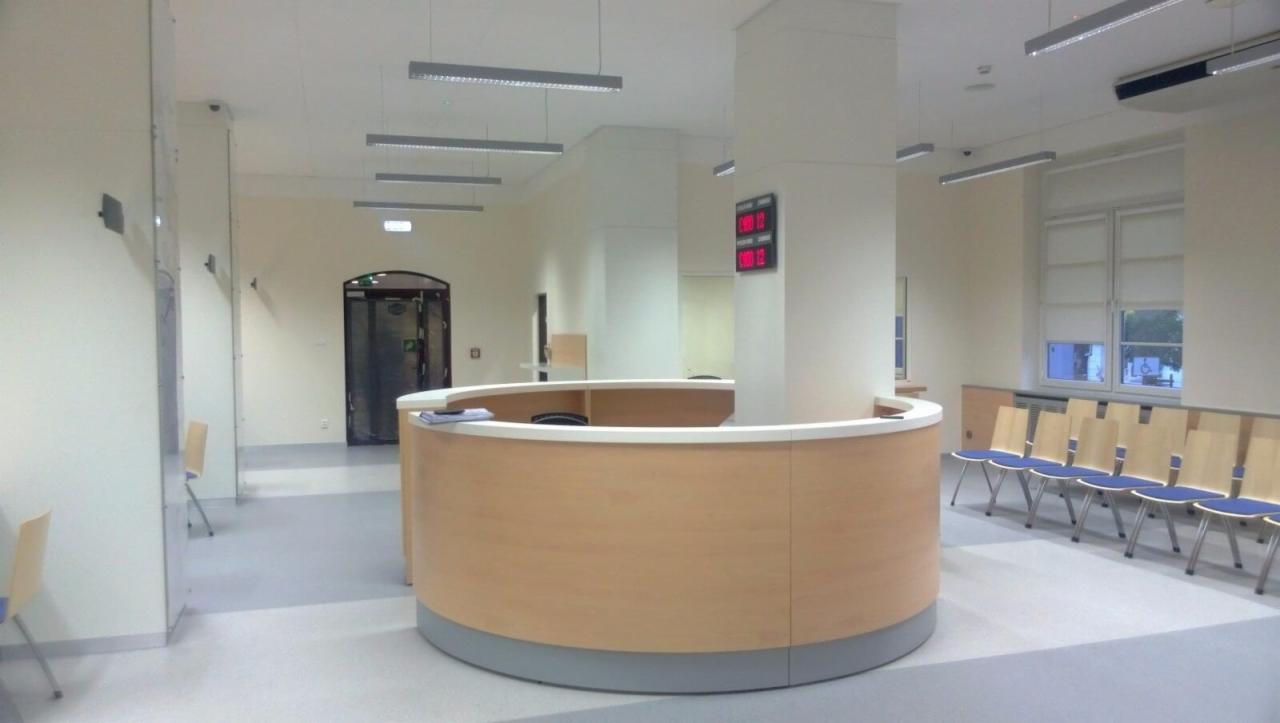 Jasne, przestronne wnętrze biura z recepcją o zaokrąglonym kształcie, rzędem krzeseł dla klientów i nowoczesnym oświetleniem sufitowym.