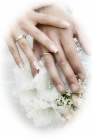 Dłonie pary młodej z obrączkami spoczywające na bukiecie ślubnym, delikatne zdobienie paznokci u kobiety.