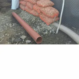 Układanie drenażu: folia kubełkowa, rura drenarska i worki z kruszywem tworzące zabezpieczenie fundamentu.