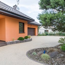 Pomarańczowy dom jednorodzinny z brązowymi akcentami i brukowanym podjazdem w Gorzowie Wielkopolskim, otoczony zielenią. Widok z zewnątrz, w słoneczny dzień.