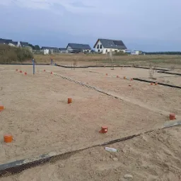 Fundamenty domu jednorodzinnego w Słupsku z widocznymi pionowymi rurami kanalizacyjnymi i zbrojeniami, przygotowane do dalszych prac budowlanych.