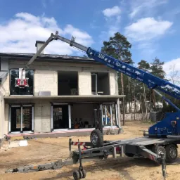 Montaż okna na elewacji domu w stanie surowym za pomocą dźwigu z platformą transportową.