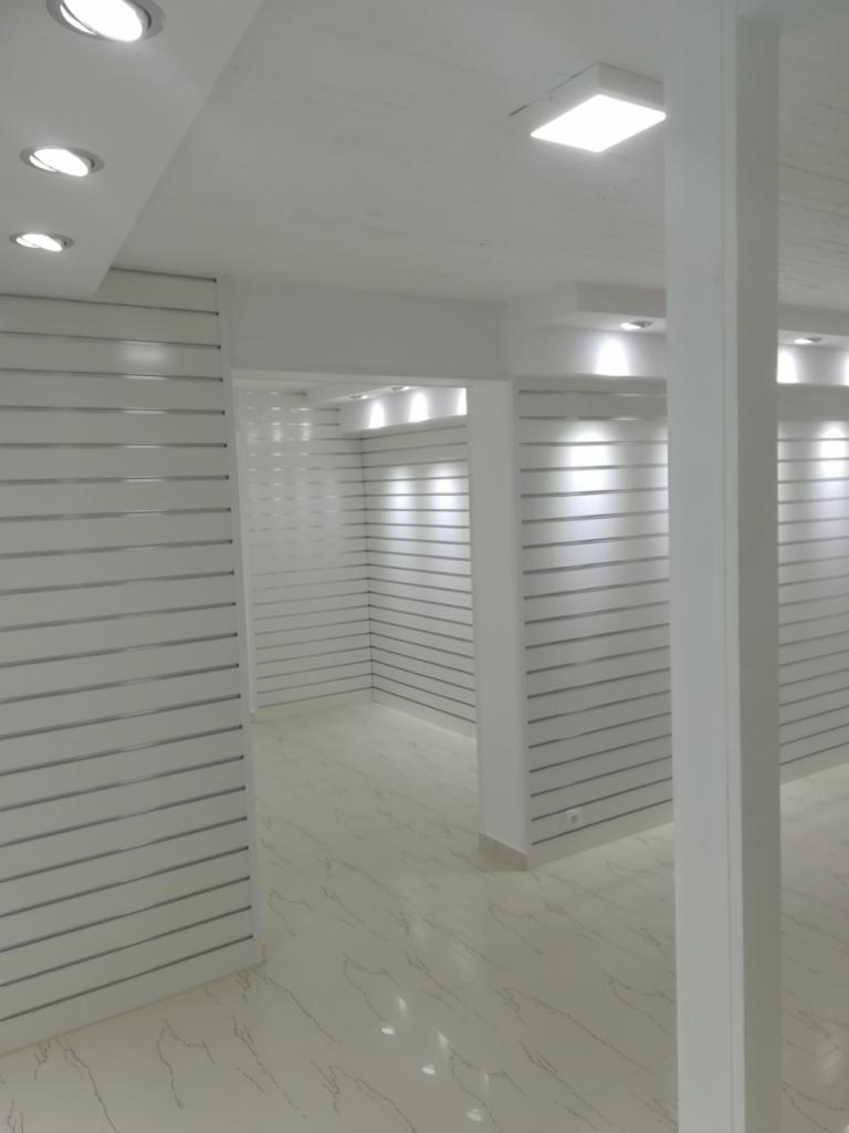 Białe, puste wnętrze sklepu z panelami ściennymi z poziomymi listwami i marmurową podłogą, oświetlone lampami sufitowymi