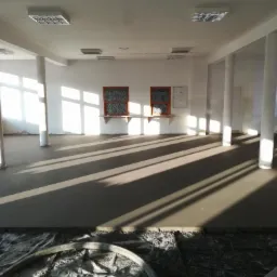 Świeżo wylana, gładka posadzka w przestronnym, jasnym pomieszczeniu z kolumnami, z widocznymi śladami węża do wylewania na folii ochronnej.