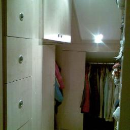 Stolpar - Wnętrze szafy na wymiar z jasnego drewna z drzwiami przesuwnymi i szufladami, widoczne ubrania na wieszakach.