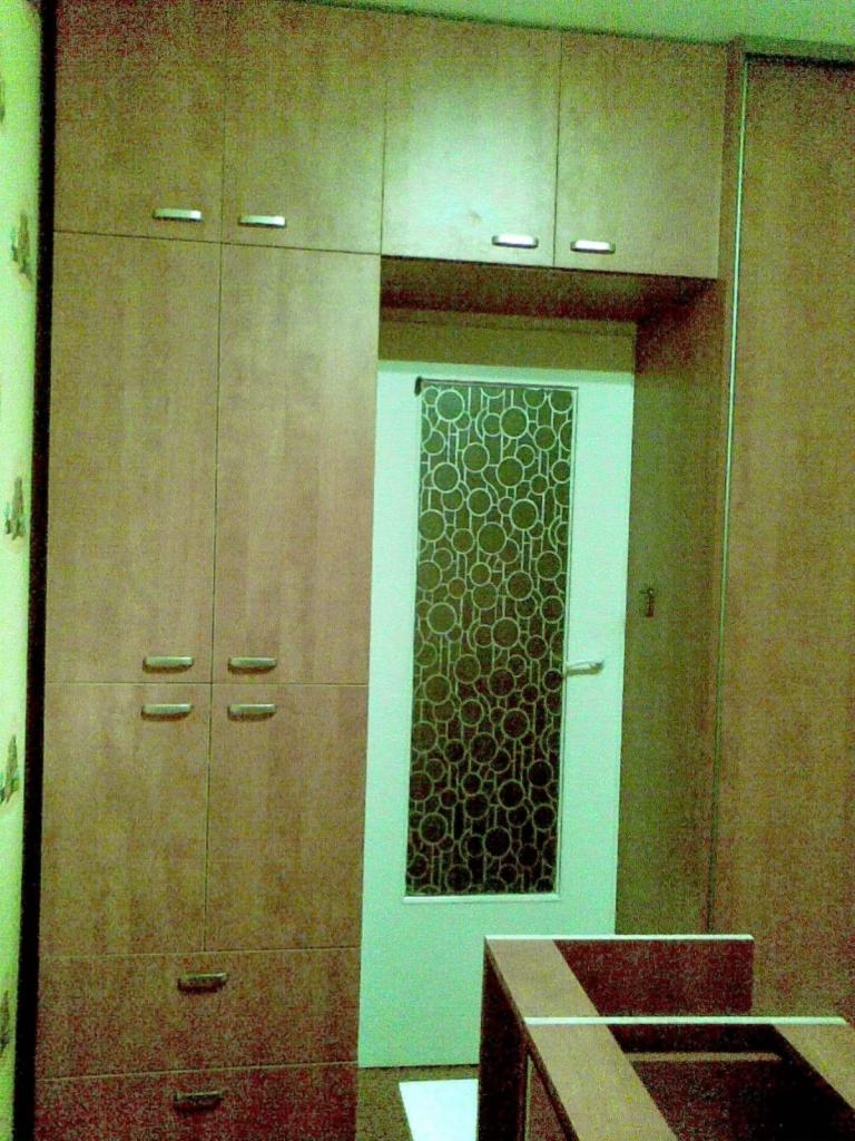 Wysoka szafa z płyty imitującej drewno, z górnymi szafkami i dolnymi szufladami, obok drzwi z szybą o wzorze z okręgów.