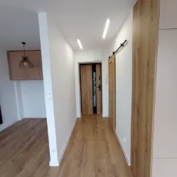 Korytarz w Zgorzałem z drewnianą podłogą, białymi ścianami i dwiema parami drzwi, z których jedna jest przesuwna.