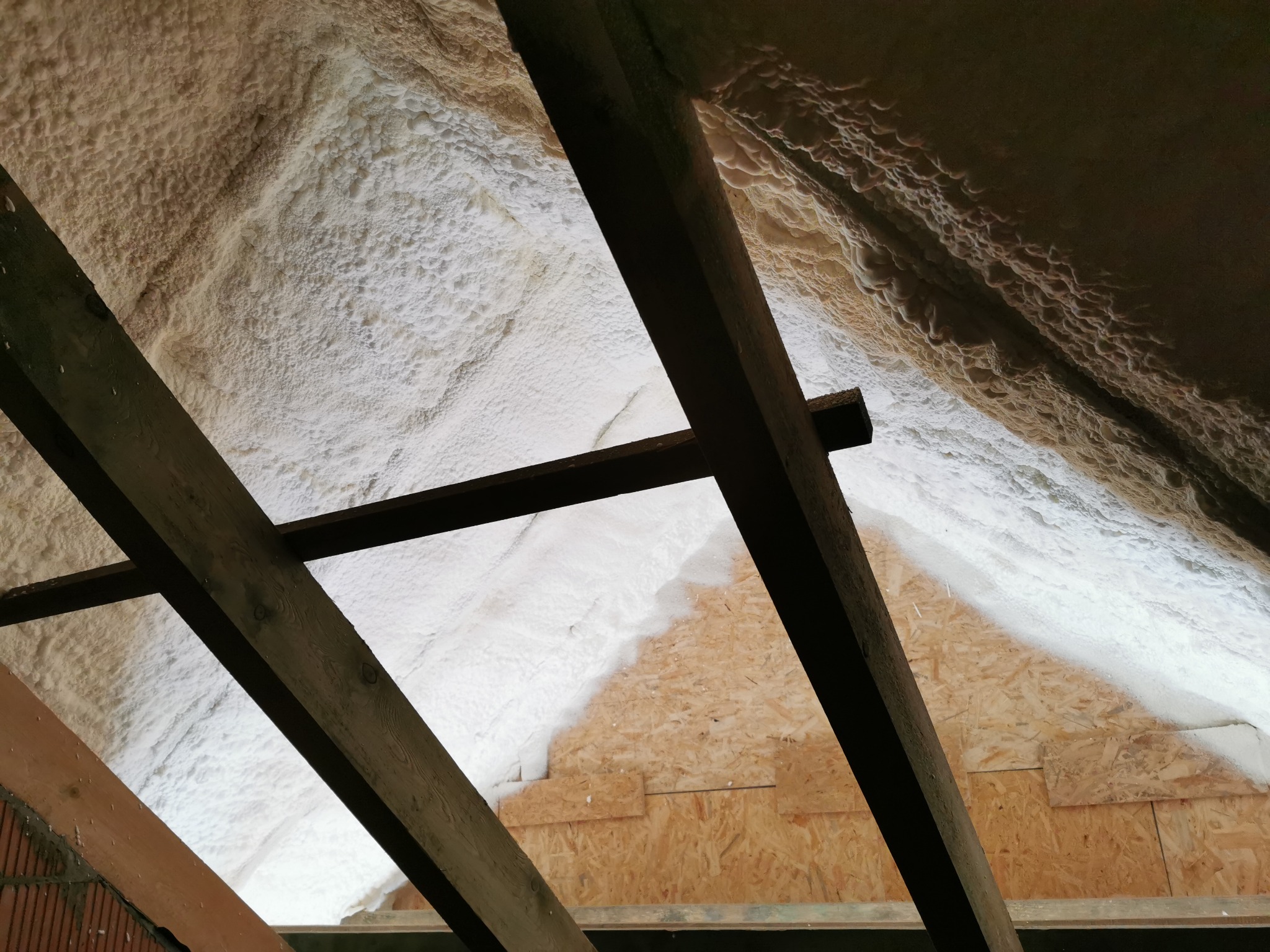 Poddasze ocieplone pianką, widoczne drewniane krokwie i fragment niezabezpieczonej płyty OSB.