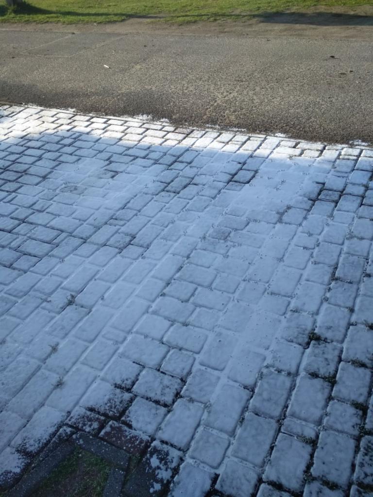 Kostka brukowa pokryta białym osadem, prawdopodobnie po czyszczeniu, z widocznym fragmentem asfaltowej drogi i trawnika w tle.