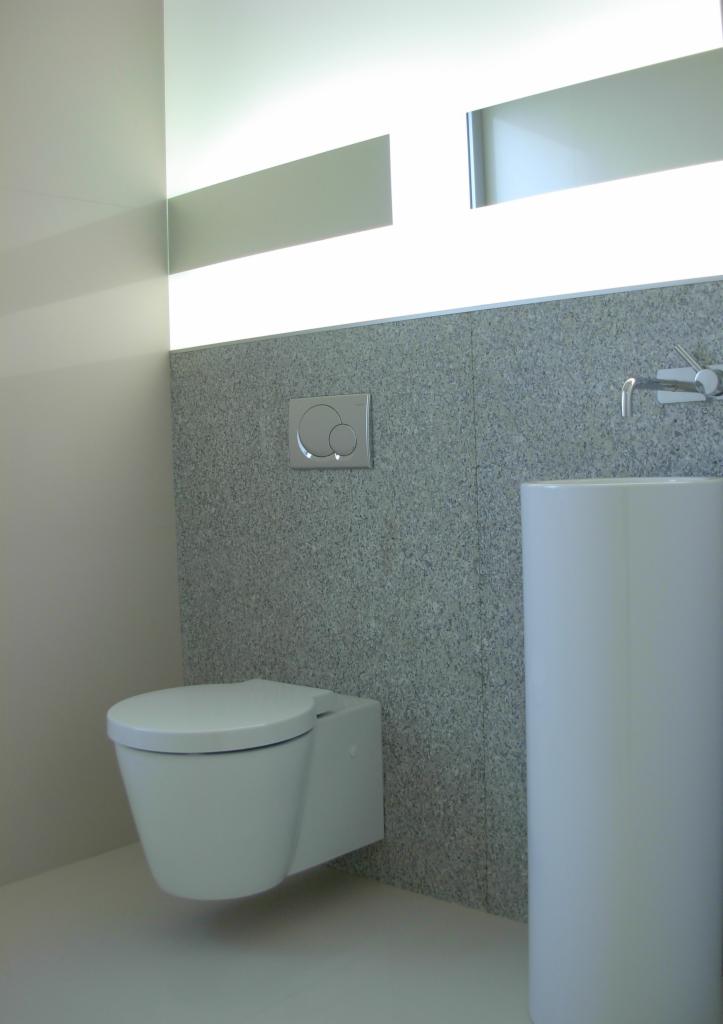 Minimalistyczna toaleta podwieszana z szarym, kamiennym panelem ściennym i podświetlanym lustrem, nowoczesna armatura łazienkowa.