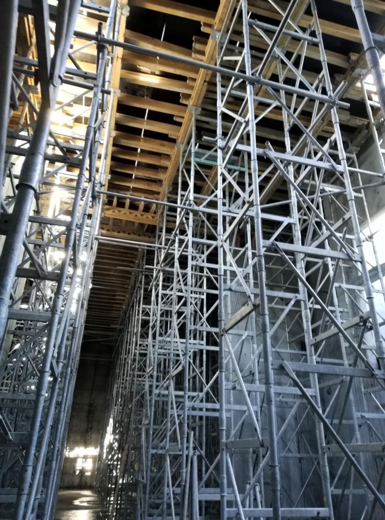 Skomplikowany system rusztowań podtrzymujących drewniane szalunki stropu na placu budowy, widok z dołu ukazujący perspektywę i konstrukcję wsporczą.
