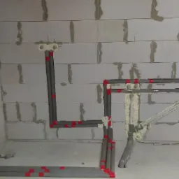 Szare rury instalacji wodnej i kanalizacyjnej zamocowane w ścianie z betonu komórkowego, zabezpieczone czerwoną taśmą, z widoczną pianką montażową.