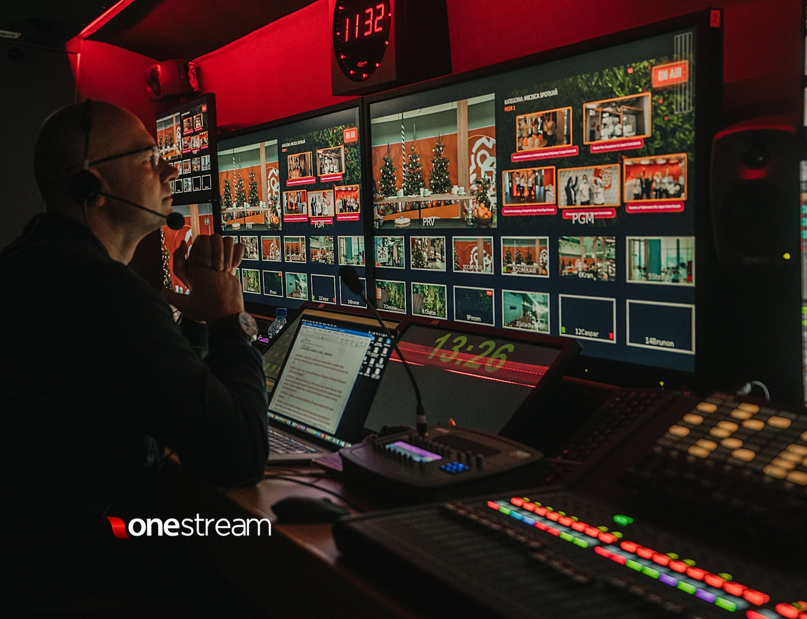 Operator w reżyserce, monitor z podglądem scen z choinkami, mikser audio, zegar cyfrowy, oświetlenie studyjne w kolorze czerwonym.