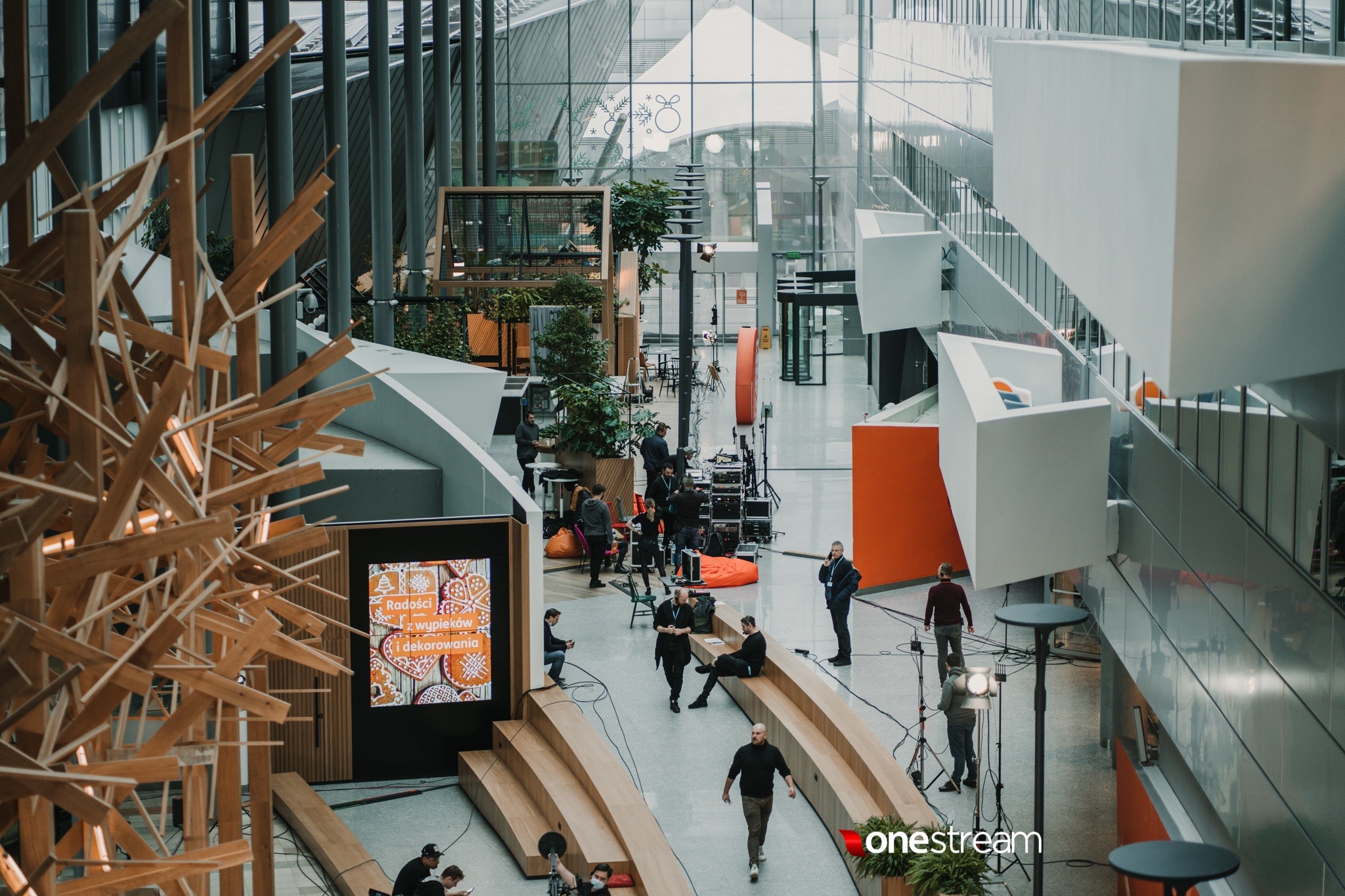 Ekipa filmowa w przestronnym, nowoczesnym wnętrzu podczas nagrywania ujęć, widoczne oświetlenie studyjne, sprzęt dźwiękowy i osoby pracujące na planie.