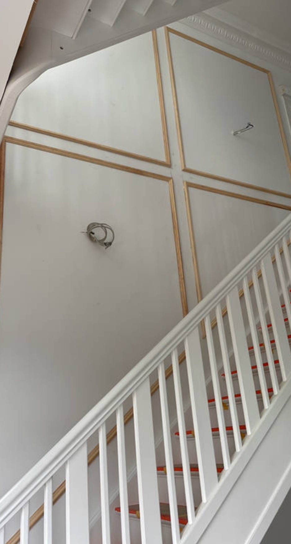 Ściana klatki schodowej z dekoracyjnymi panelami w trakcie montażu, widoczne przewody elektryczne, białe balustrady schodów.