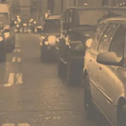 Korek uliczny z widocznymi samochodami i światłami w oddali, obok logo i napis 'Ośrodek Pomocy Poszkodowanym w Wypadkach' na beżowym tle.