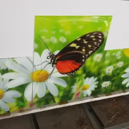 Szklane panele z nadrukiem motyla i białych kwiatów, ułożone obok siebie, widoczne na stanowisku roboczym.