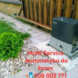 Zamontowany napęd bramy przesuwnej Beninca z widoczną listwą zębatą i kluczykiem w zamku, na tle drewnianego ogrodzenia i kostki brukowej.